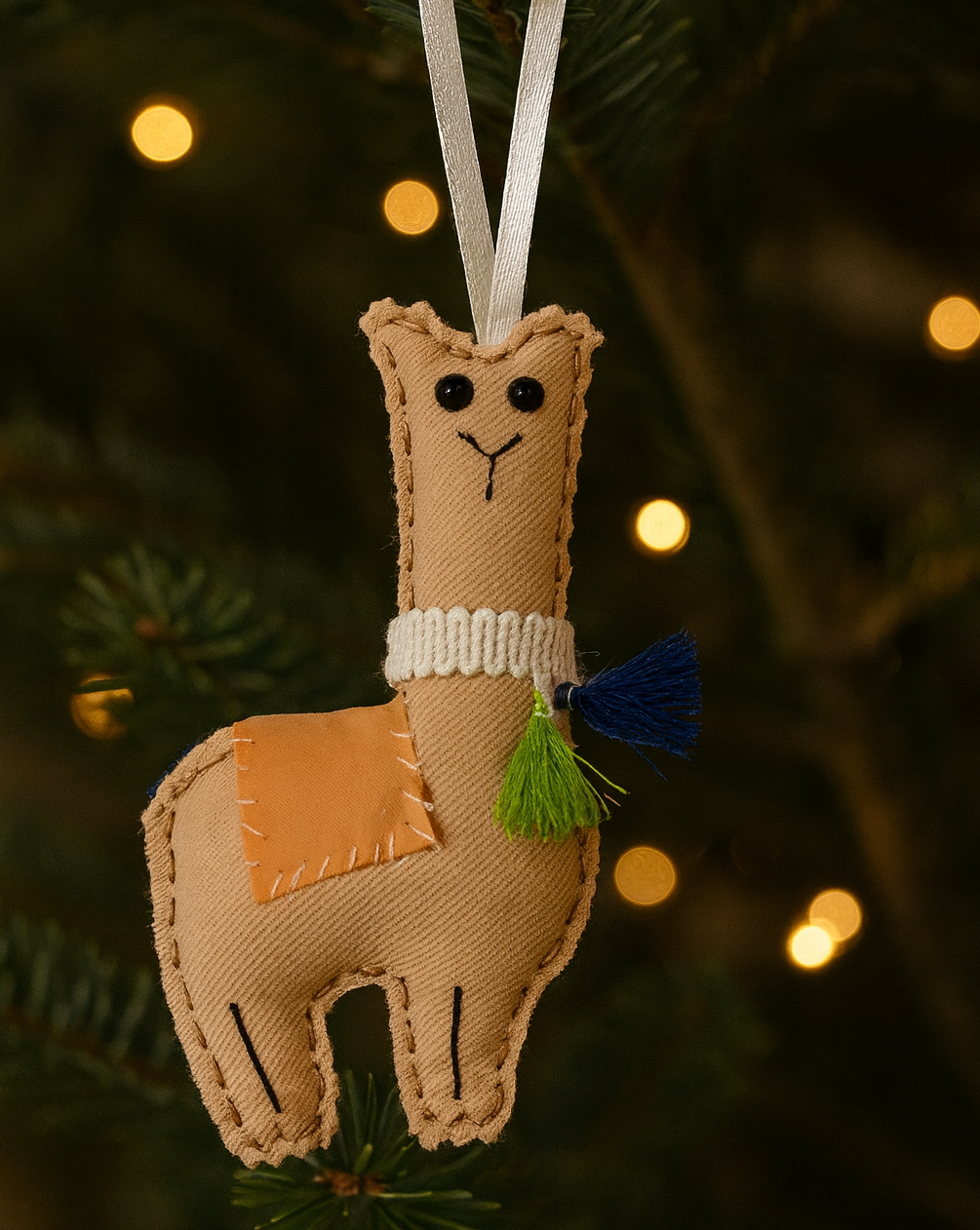 Felt llama ornament hanging on a Christmas tree with blurred lights in the background