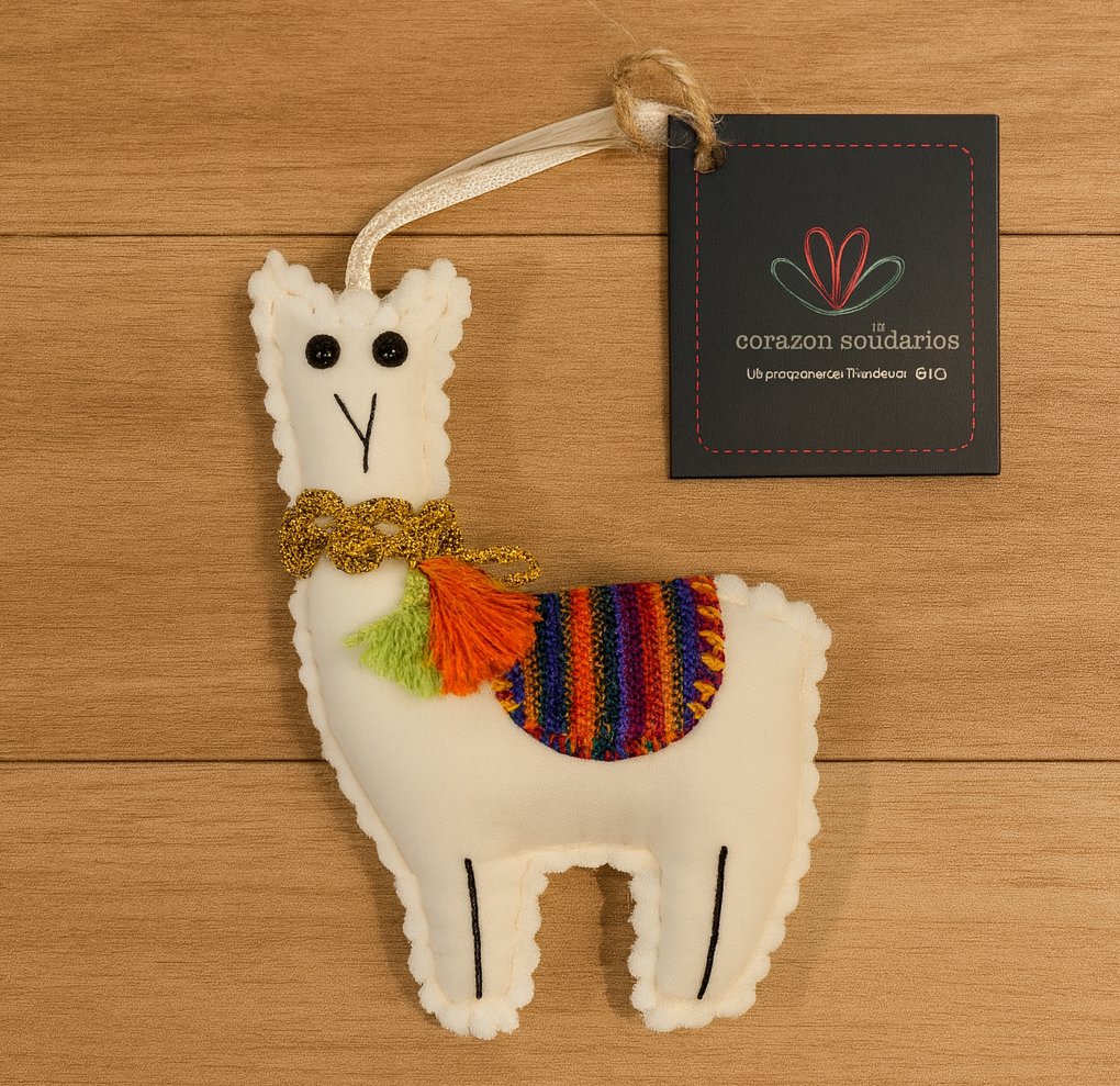 White llama ornament with colorful saddle and bow tie on a wooden surface, accompanied by a 'corazones solidarios' tag.